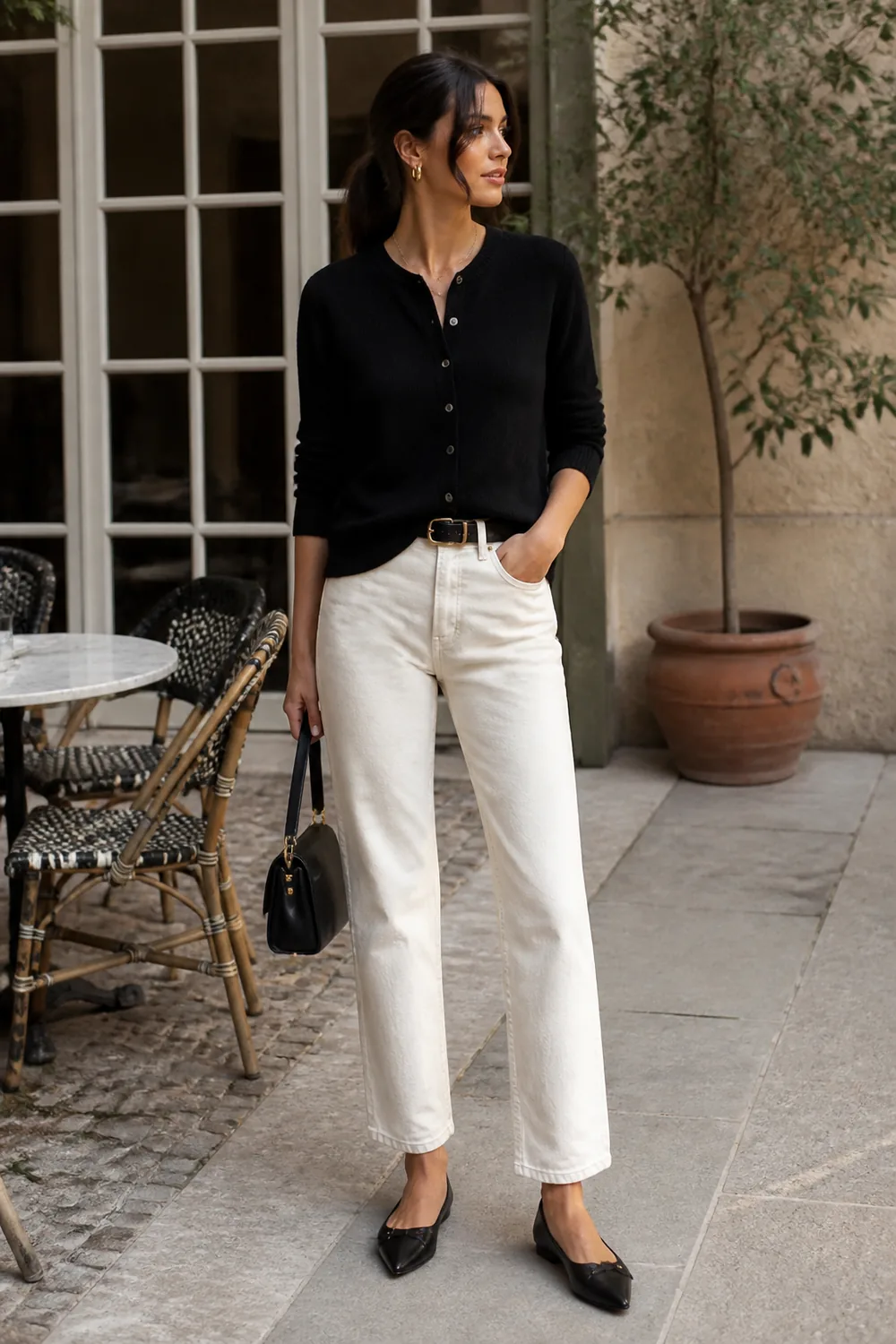 A fine black cardigan worn as a top, ecru jeans, and black pointed flats