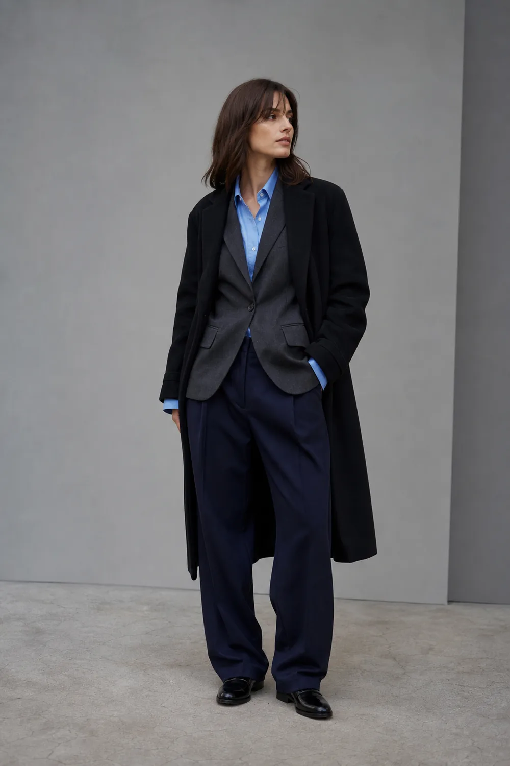 A charcoal blazer over a blue shirt beneath a black wool coat with navy trousers